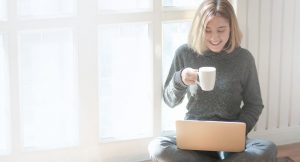 Female holding white mug looking at laptop