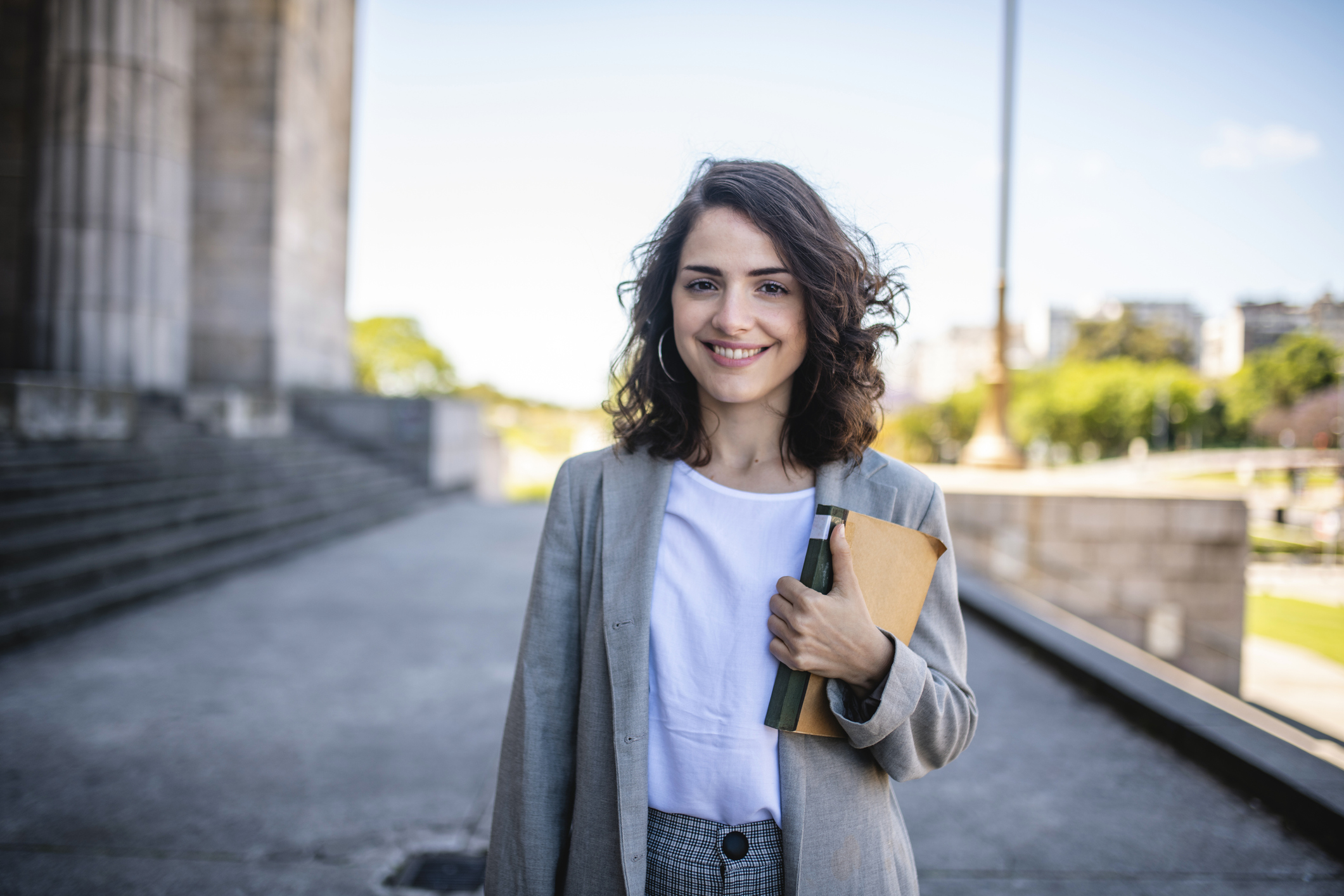Female smiling holding a book in front of building